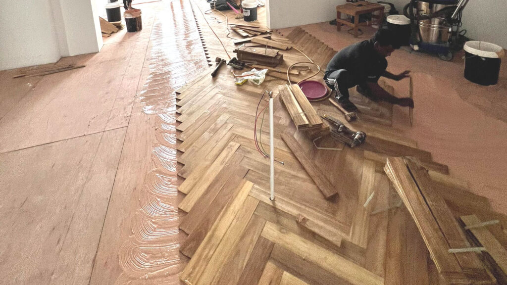 A professional installing hardwood floors in a living room.